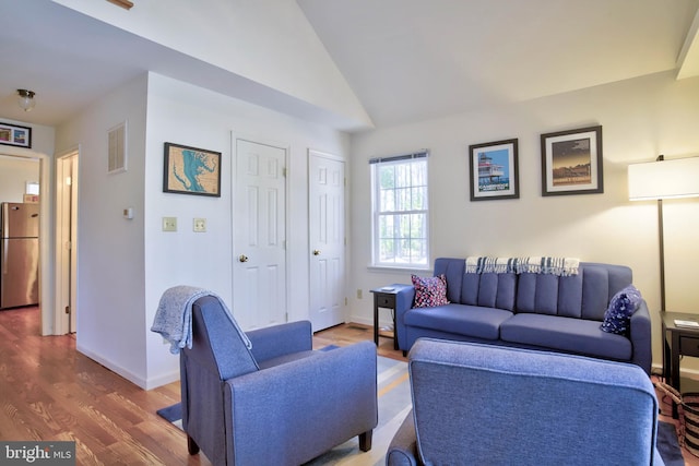 living area with visible vents, wood finished floors, baseboards, and vaulted ceiling