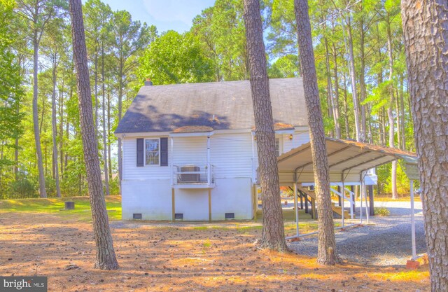 back of house with crawl space, a shingled roof, and a carport