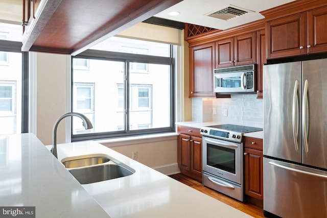 kitchen featuring appliances with stainless steel finishes, decorative backsplash, sink, and light hardwood / wood-style flooring