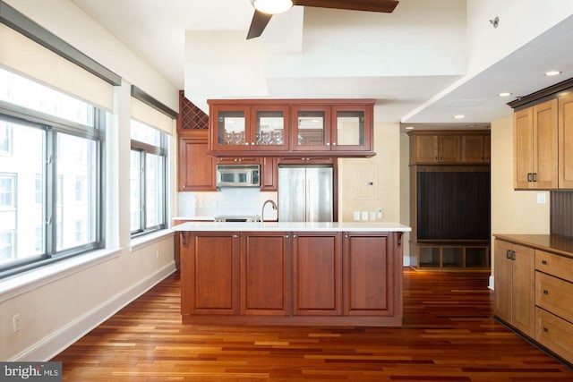 kitchen with a center island with sink, dark wood-type flooring, stainless steel appliances, and ceiling fan