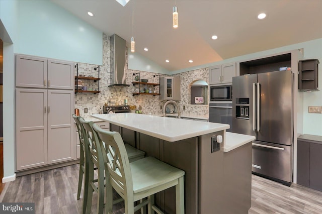 kitchen with light wood-type flooring, tasteful backsplash, stainless steel appliances, a breakfast bar, and wall chimney exhaust hood