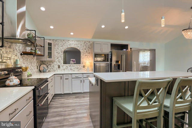 kitchen with light hardwood / wood-style floors, stainless steel refrigerator with ice dispenser, a breakfast bar area, black range with electric stovetop, and wall chimney range hood