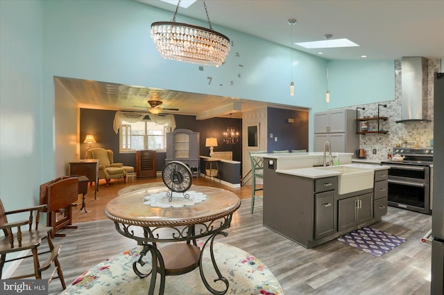 kitchen with wall chimney exhaust hood, a center island with sink, sink, ceiling fan, and stainless steel range with electric cooktop