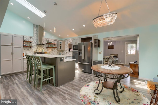 kitchen featuring a skylight, a kitchen breakfast bar, a kitchen island, stainless steel fridge with ice dispenser, and wall chimney range hood