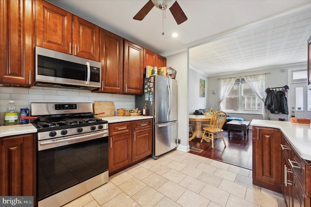 kitchen featuring light countertops, decorative backsplash, appliances with stainless steel finishes, ornamental molding, and ceiling fan