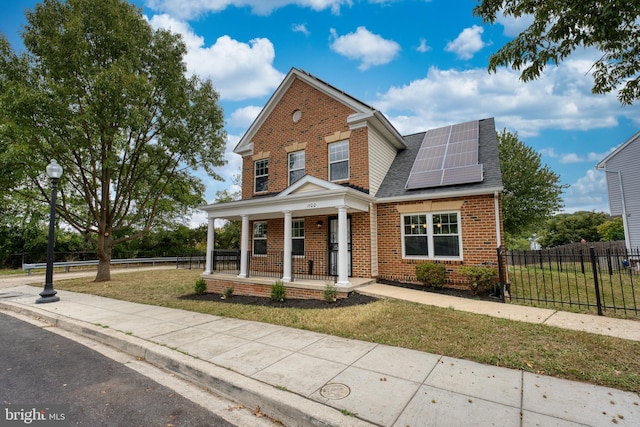 traditional-style home with fence, solar panels, covered porch, a front lawn, and brick siding