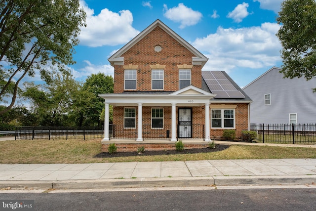 view of front of home with roof mounted solar panels, brick siding, a porch, and fence