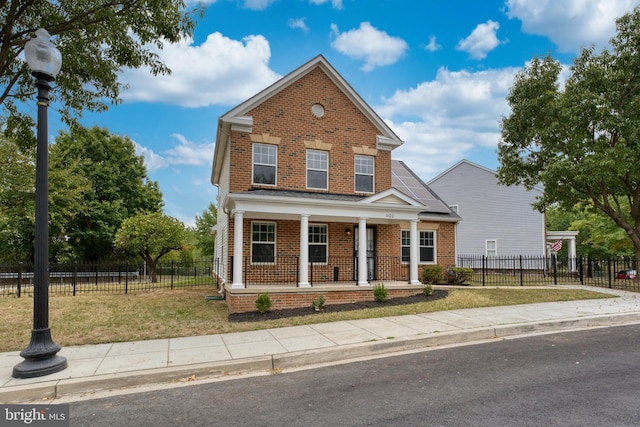 traditional-style home featuring brick siding, covered porch, a front lawn, and fence