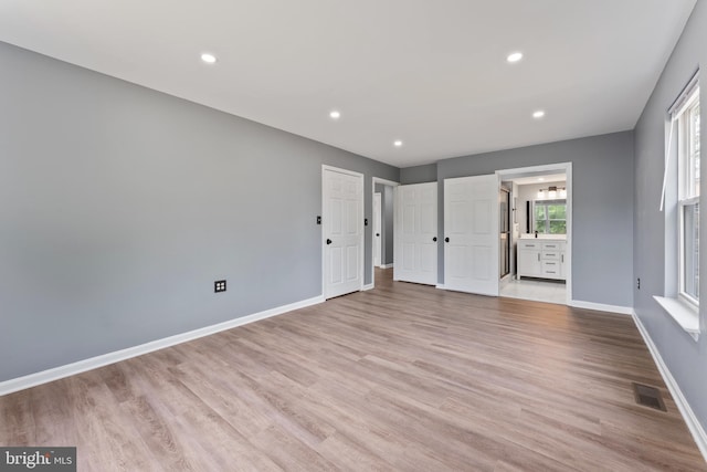 unfurnished bedroom featuring ensuite bath and light hardwood / wood-style floors