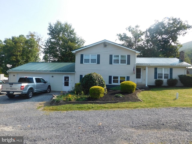 tri-level home featuring gravel driveway, metal roof, a chimney, and a front lawn