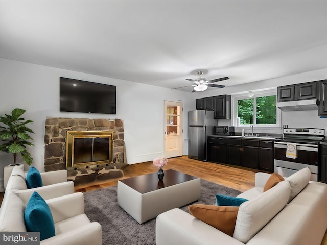 living room featuring light hardwood / wood-style floors, ceiling fan, sink, and a fireplace