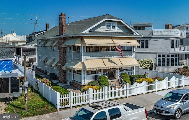 view of front of property with a fenced front yard, a residential view, covered porch, and roof with shingles