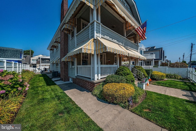 view of side of property with a balcony, fence, cooling unit, and a yard