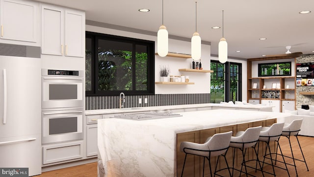 kitchen with light stone counters, stainless steel double oven, a sink, white refrigerator, and light wood finished floors