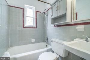 full bathroom with tile walls, tiled shower / bath, toilet, and sink