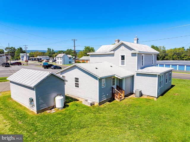 rear view of property with central air condition unit, entry steps, an outbuilding, and a yard