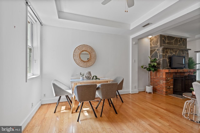 dining area featuring a raised ceiling, ceiling fan, hardwood / wood-style floors, and a stone fireplace