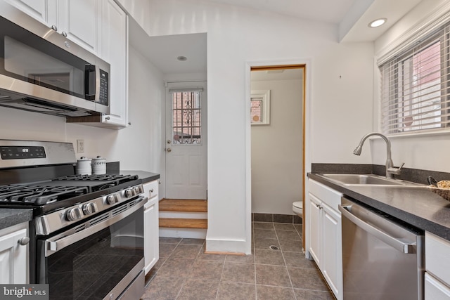 kitchen featuring a sink, white cabinets, appliances with stainless steel finishes, dark countertops, and dark tile patterned floors