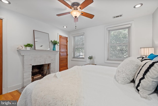 bedroom with a fireplace, ceiling fan, and light hardwood / wood-style floors