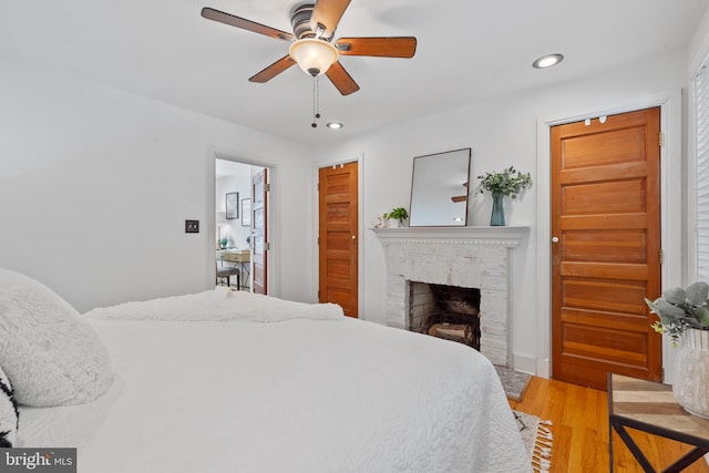 bedroom featuring wood-type flooring, a brick fireplace, and ceiling fan