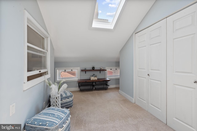 interior space featuring vaulted ceiling with skylight, light colored carpet, and plenty of natural light