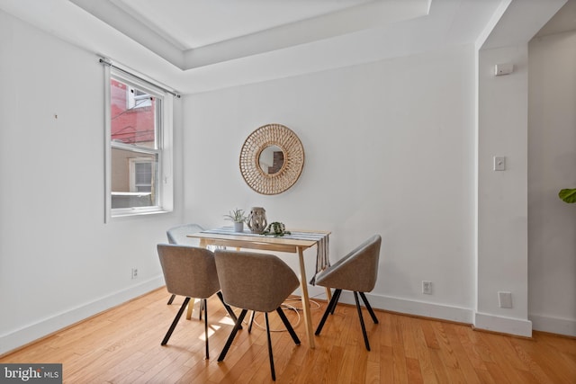 dining area with light wood-type flooring and a raised ceiling