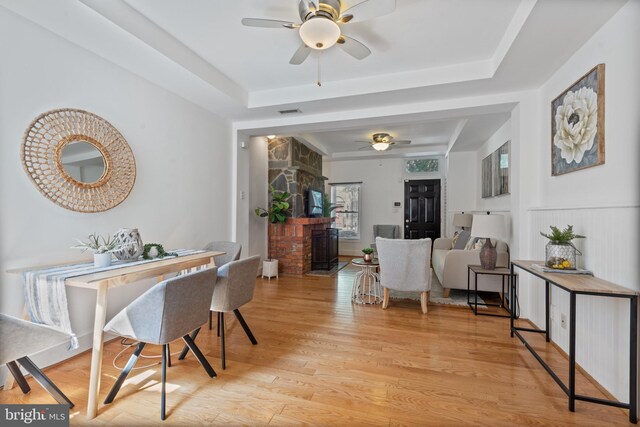 dining area featuring a fireplace, ceiling fan, a tray ceiling, and light hardwood / wood-style floors