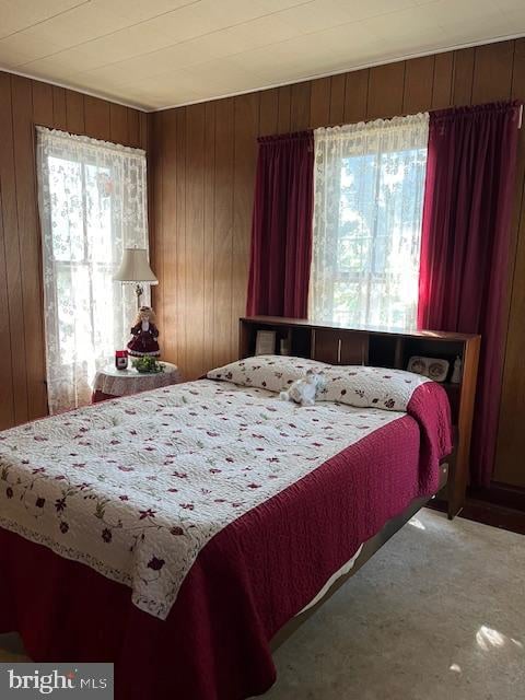 bedroom featuring multiple windows, wooden walls, and carpet