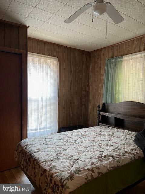 bedroom with hardwood / wood-style flooring, ceiling fan, and wooden walls