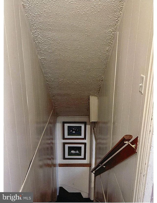 staircase with a textured ceiling and wood walls