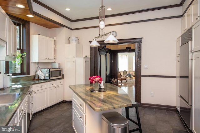 kitchen with a kitchen breakfast bar, white cabinetry, built in refrigerator, pendant lighting, and ornamental molding