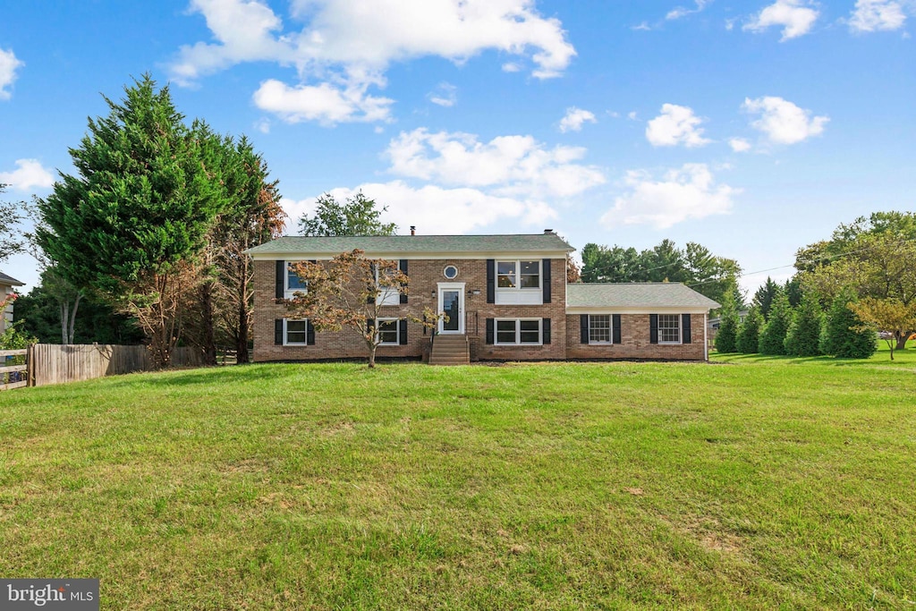 bi-level home with brick siding, a front yard, and fence