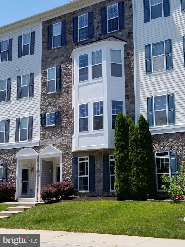 townhome / multi-family property featuring a front yard and stone siding