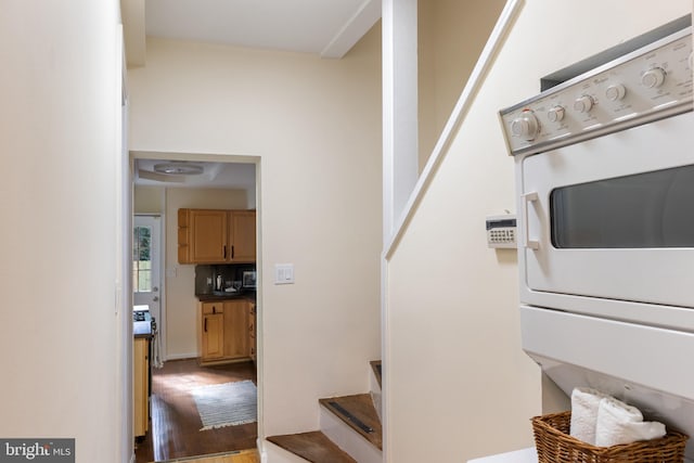 stairs with hardwood / wood-style floors and stacked washer and dryer