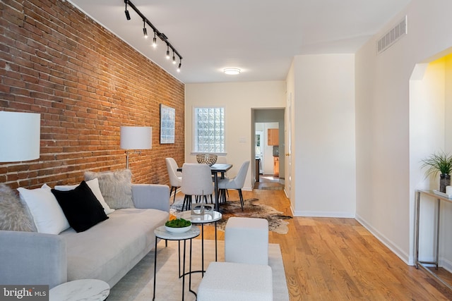 living room with light hardwood / wood-style floors, brick wall, and track lighting