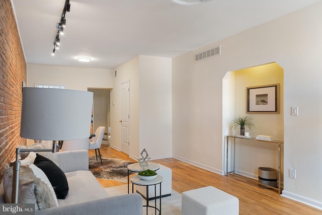 living room featuring light hardwood / wood-style flooring, rail lighting, and brick wall