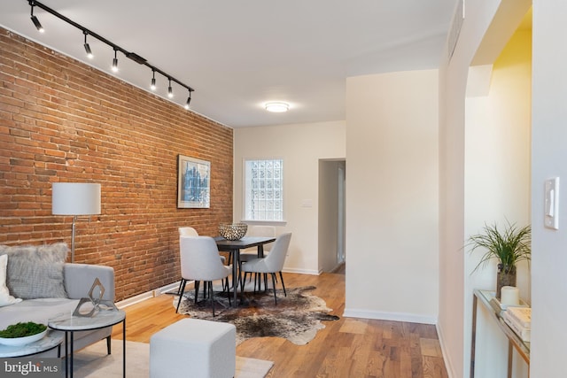 dining room featuring wood-type flooring and brick wall