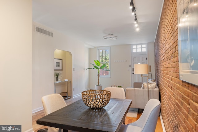 dining room with brick wall, track lighting, and hardwood / wood-style flooring