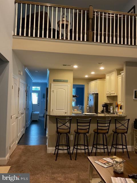 kitchen featuring dark carpet, stainless steel fridge, a breakfast bar, kitchen peninsula, and white cabinetry