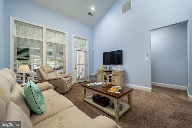 carpeted living area with visible vents, a healthy amount of sunlight, high vaulted ceiling, and baseboards