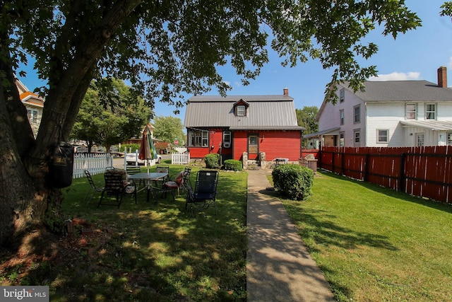 rear view of property with metal roof, a fenced backyard, a gambrel roof, a yard, and a chimney