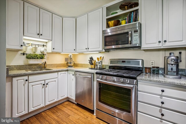 kitchen with light hardwood / wood-style flooring, stone countertops, stainless steel appliances, sink, and white cabinetry