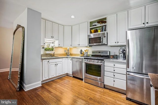 kitchen with white cabinetry, light stone counters, sink, appliances with stainless steel finishes, and light hardwood / wood-style floors