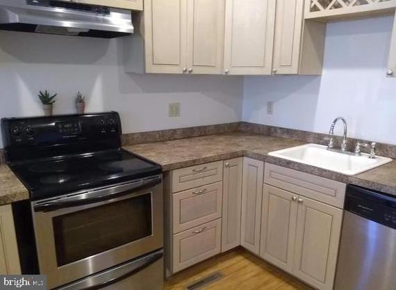 kitchen featuring appliances with stainless steel finishes, light hardwood / wood-style floors, ventilation hood, cream cabinets, and sink