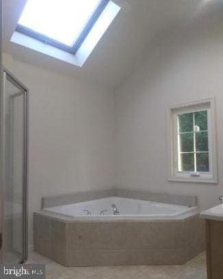 bathroom featuring independent shower and bath, vaulted ceiling with skylight, vanity, and tile patterned floors