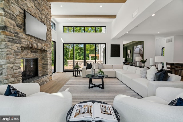 living room featuring beam ceiling, light hardwood / wood-style flooring, a stone fireplace, and a high ceiling