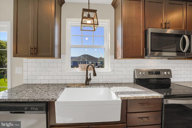 kitchen with light stone counters, sink, decorative backsplash, appliances with stainless steel finishes, and decorative light fixtures