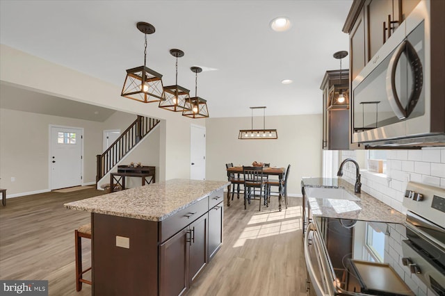 kitchen with tasteful backsplash, stainless steel microwave, dark brown cabinetry, a kitchen bar, and light wood-type flooring