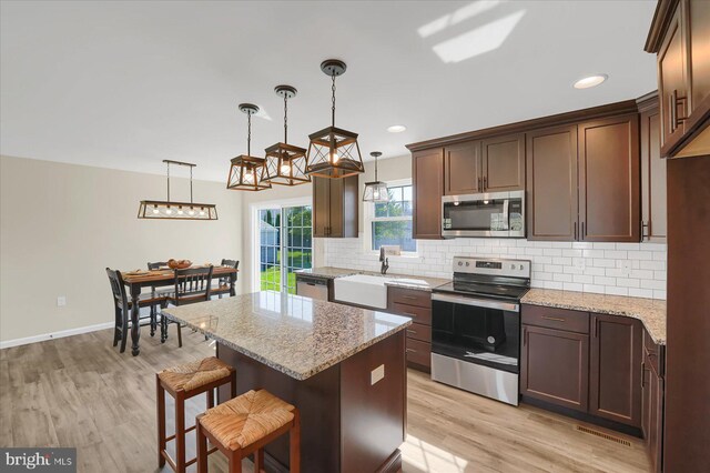 kitchen with light stone counters, decorative light fixtures, appliances with stainless steel finishes, and light wood-type flooring