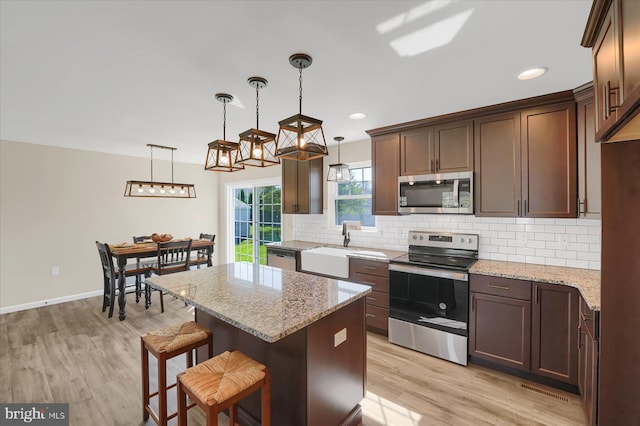 kitchen featuring stainless steel appliances, light stone countertops, backsplash, and light wood-style flooring
